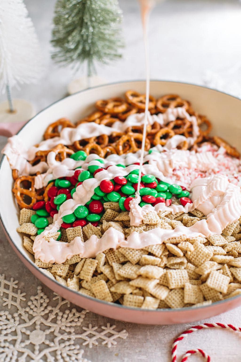 chex mix cereal, pretzels, m&ms and peppermint candies in large bowl drizzled with white chocolate