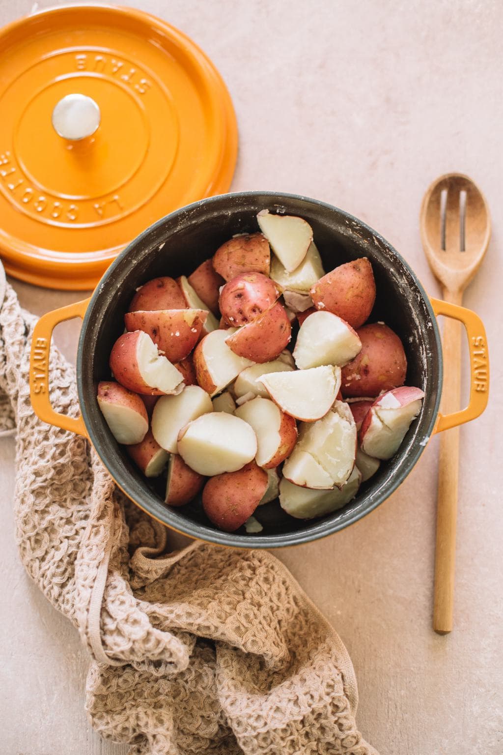 cubed red potatoes in yellow dutch oven with tan kitchen towel and wooden spoon