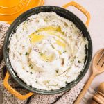 garlic mashed red potatoes in yellow dutch oven with melted butter, wooden spoon and pepper mill on side