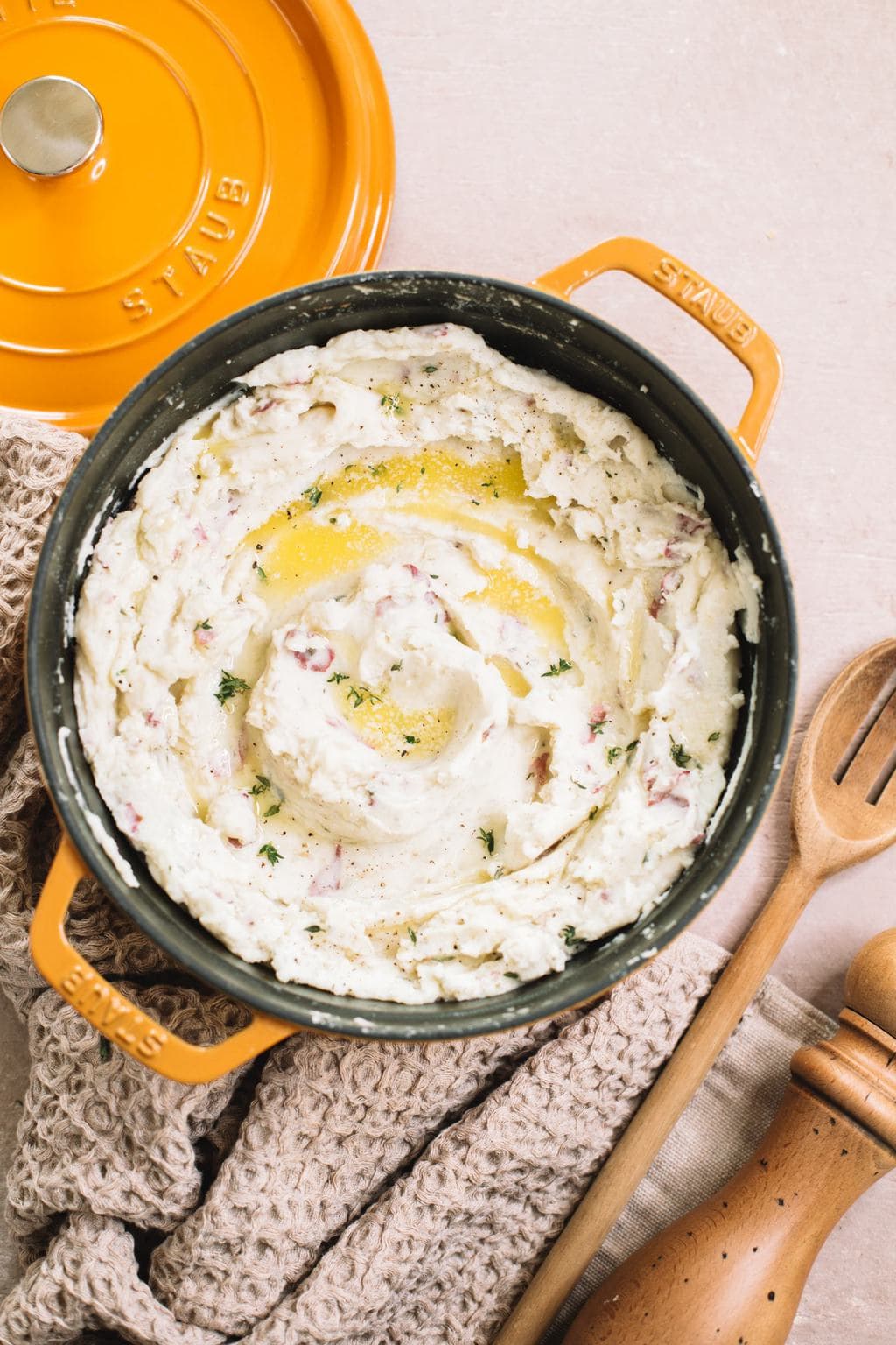 garlic mashed red potatoes in yellow dutch oven with melted butter, wooden spoon and pepper mill on side