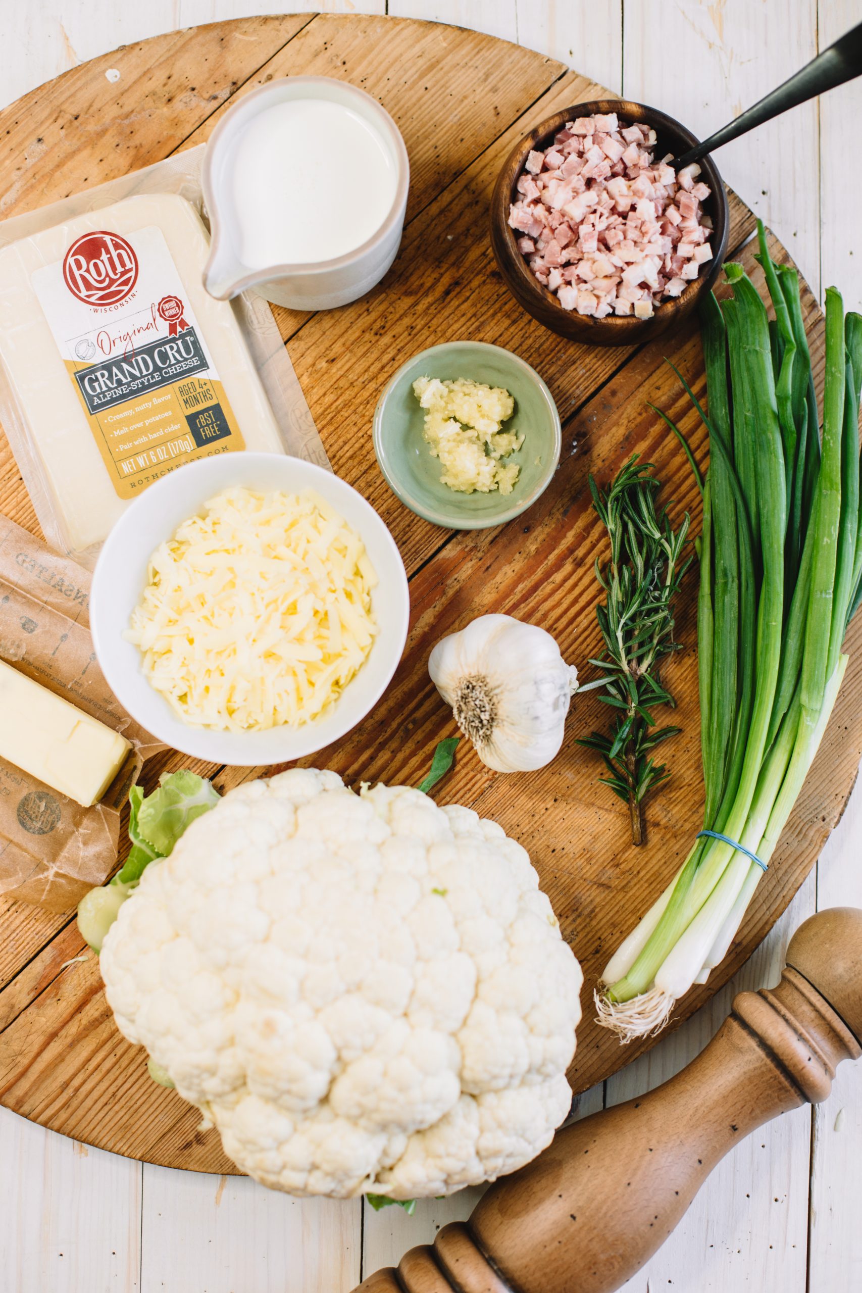 cauliflower, shredded cheese, garlic, rosemary, scallions, pancetta, cream, butter on wooden cutting board