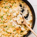 wooden spoon scooping easy cheesy cauliflower bake with pancetta in cast iron skillet