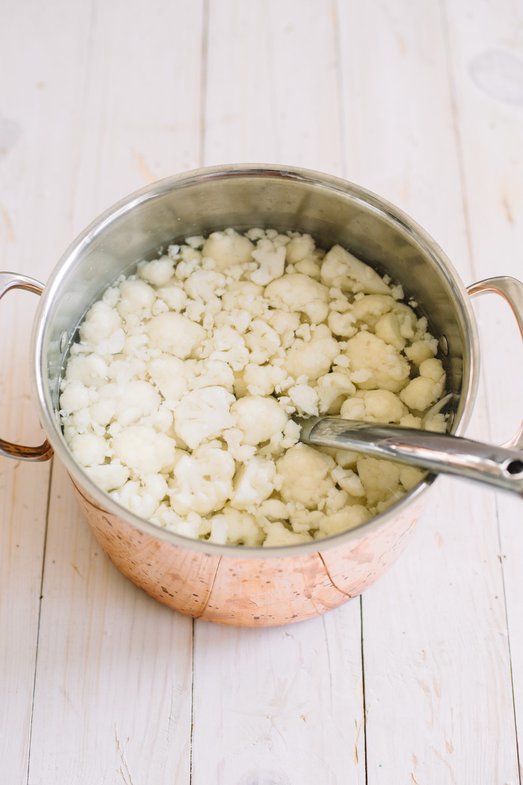 cauliflower florets with water in copper pot with stainless steel spoon