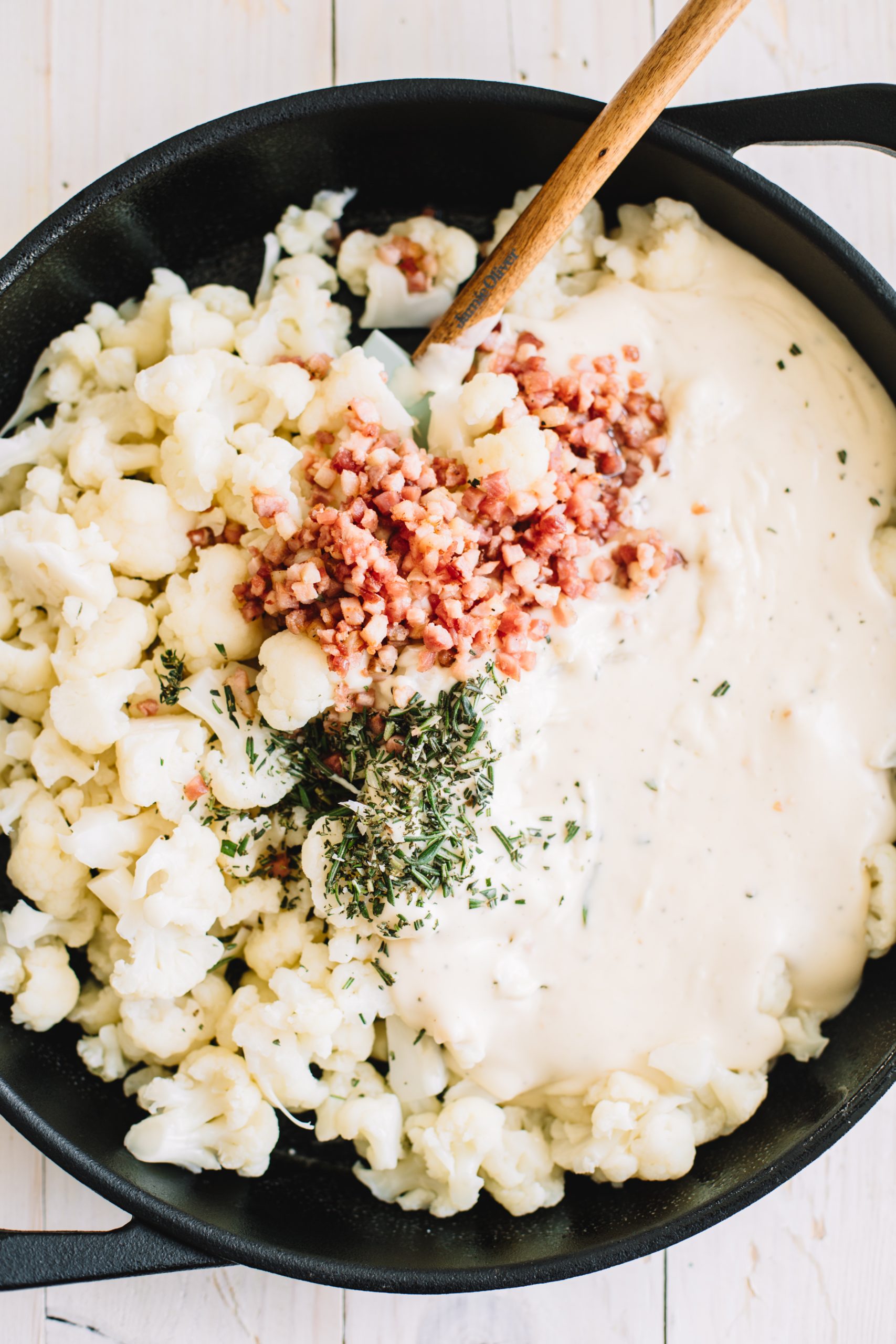 cauliflower, cheese, rosemary, thyme and pancetta in cast iron skillet with wooden spoon