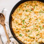 cheesy cauliflower bake with pancetta in cast iron skillet with wooden spoon on kitchen towel