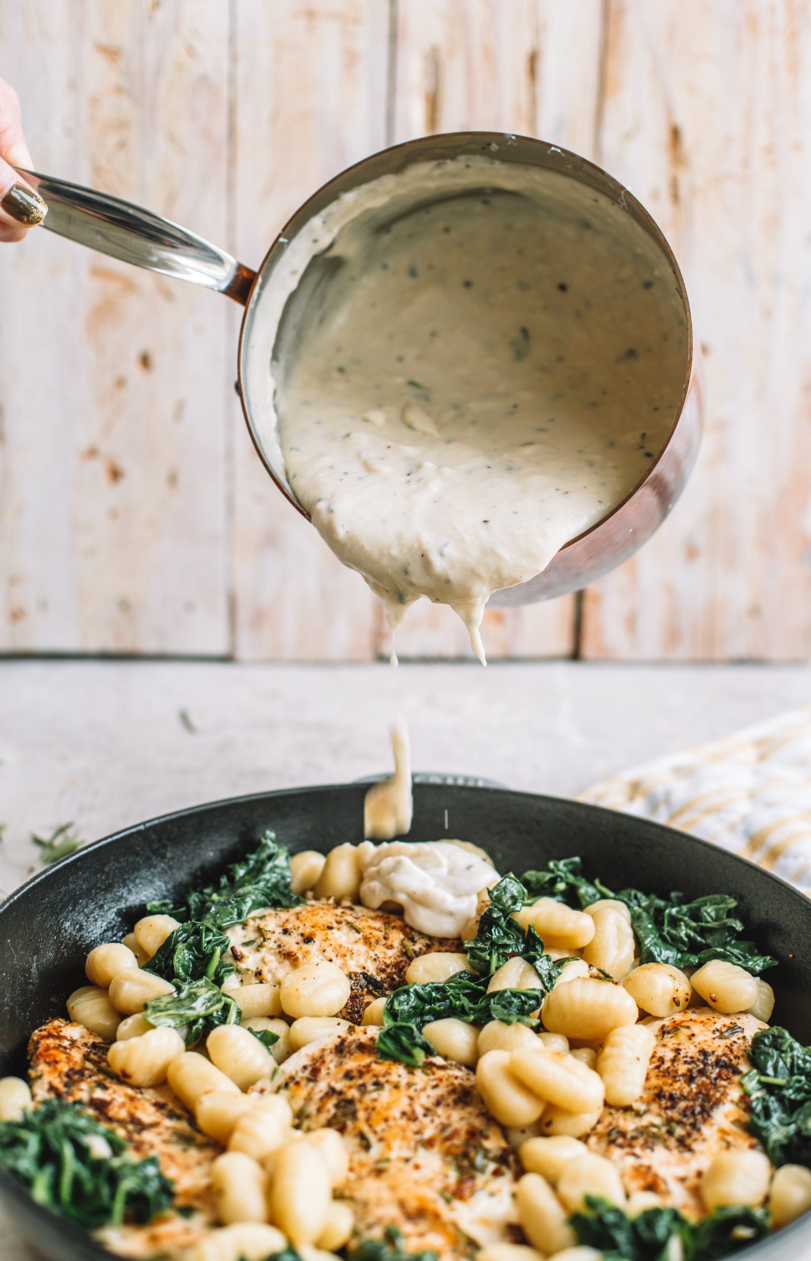 pouring cream sauce on top of chicken and gnocchi in skillet