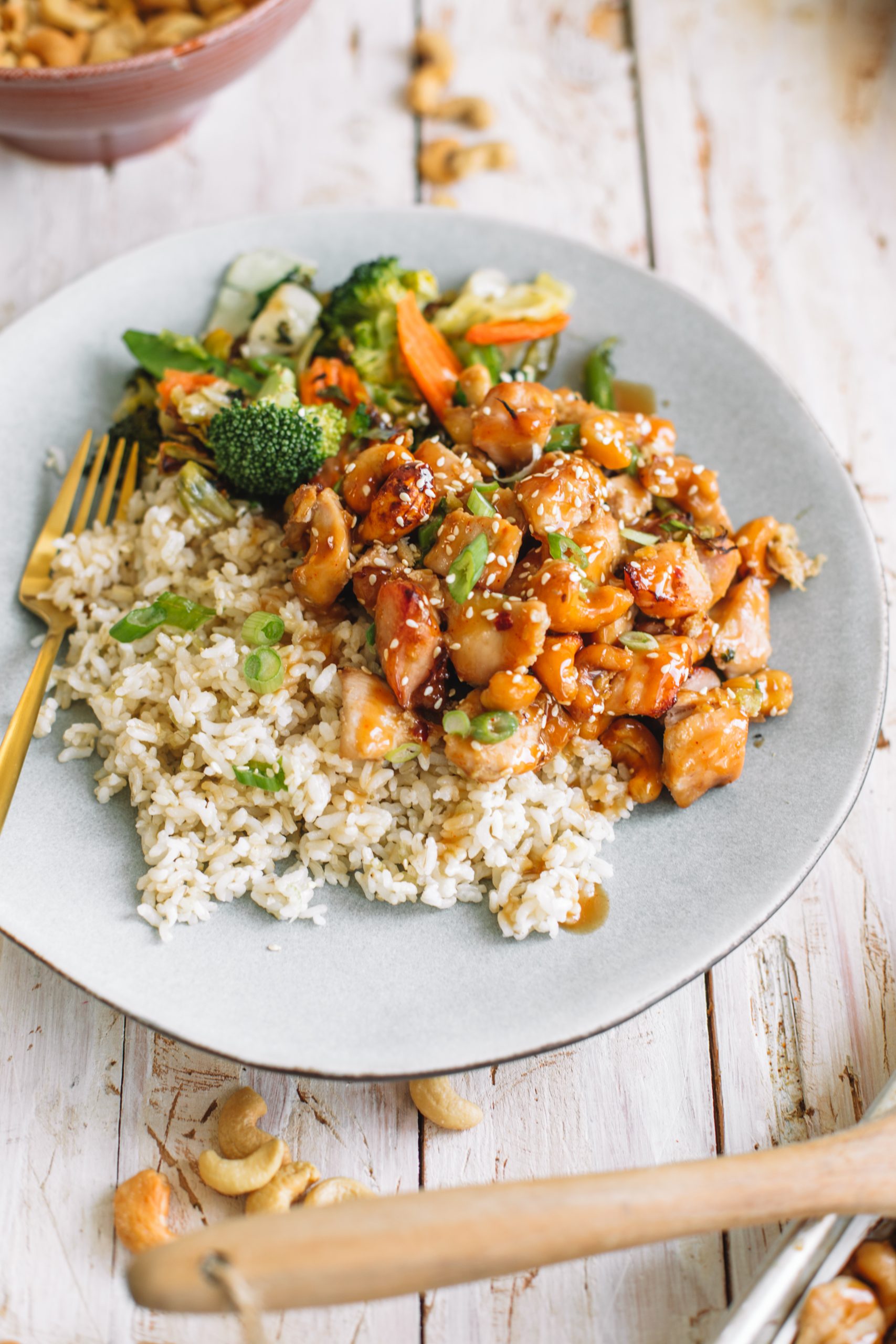 A blue plate of cashew chicken, asian style vegetables and brown rice.