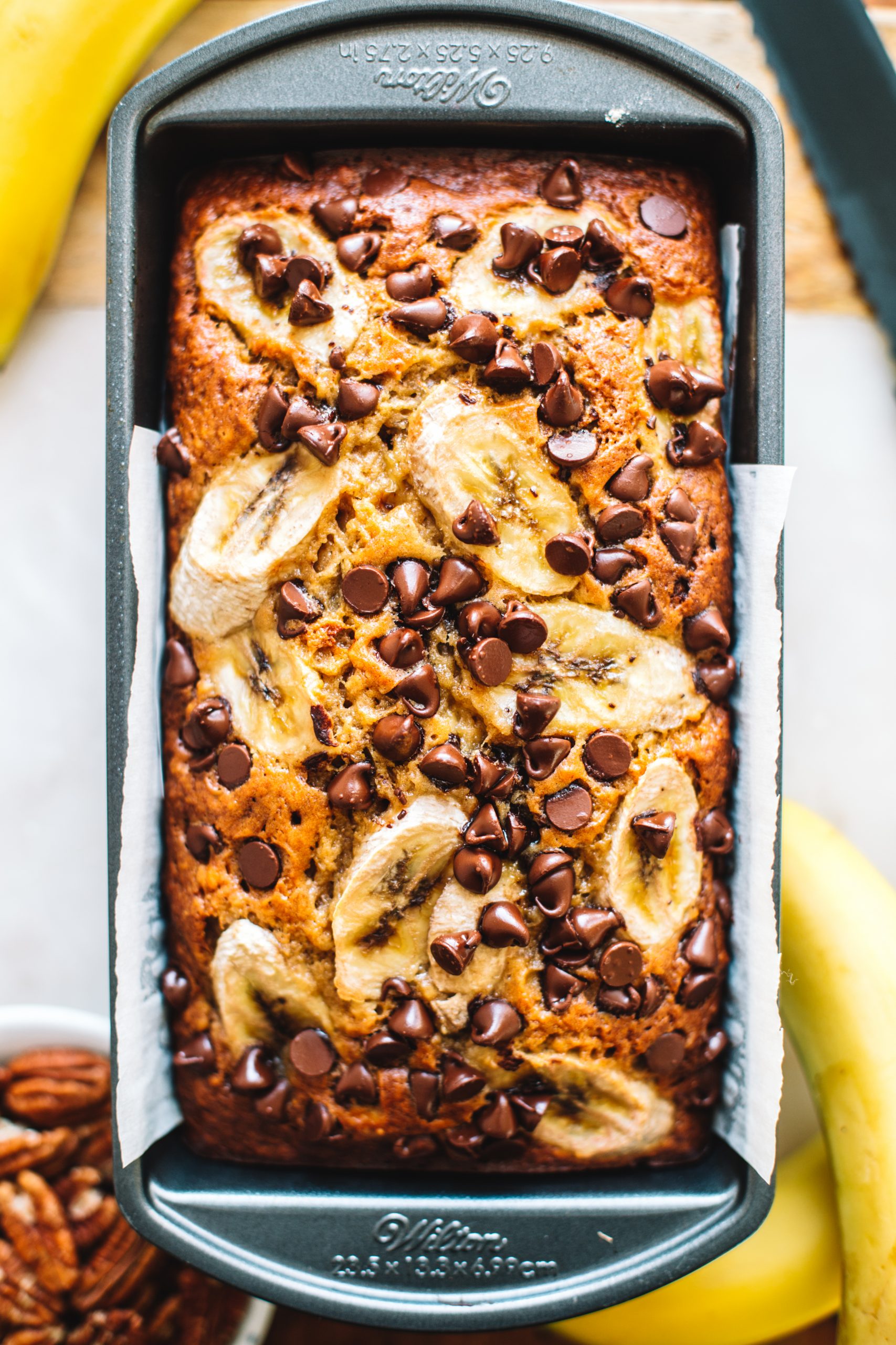 banana bread recipe topped with banana slices and chocolate chips in loaf tin