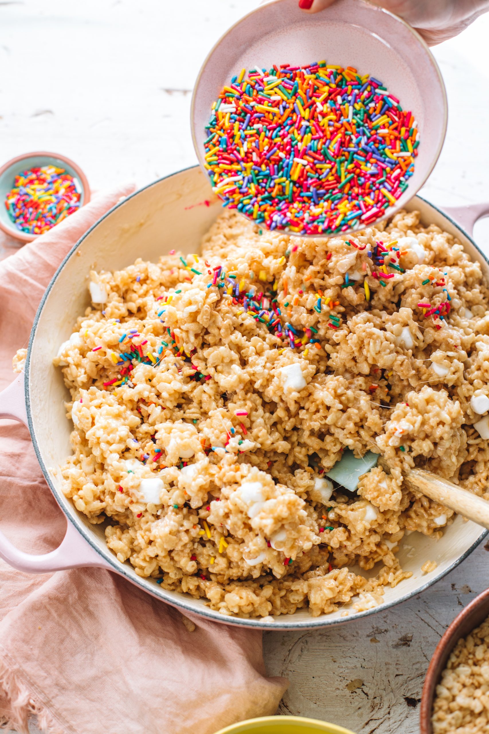 Rainbow sprinkles being poured into a batch of rice krispie treats.