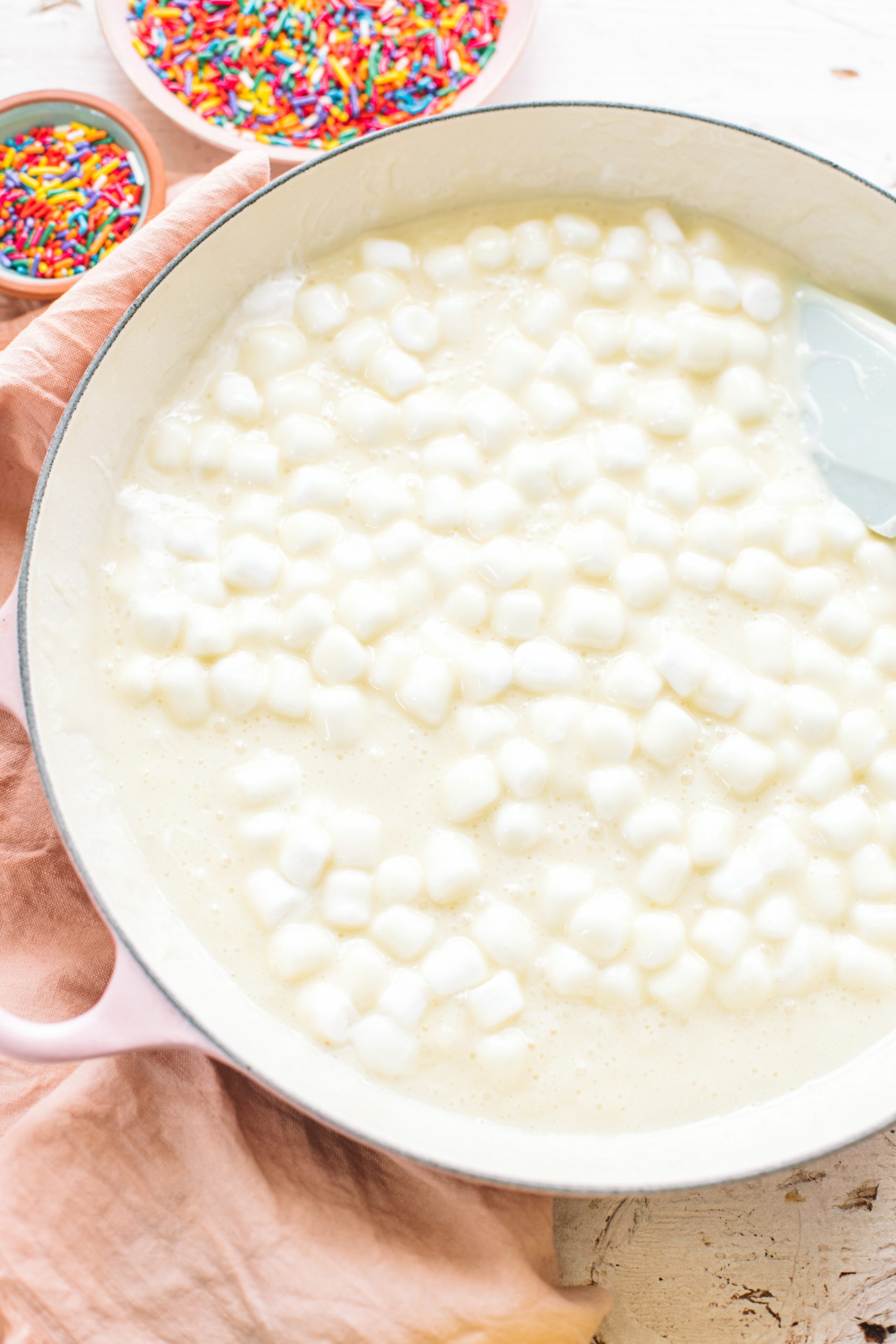 A shallow pink braiser with melted marshmallows for rice krispie treats.