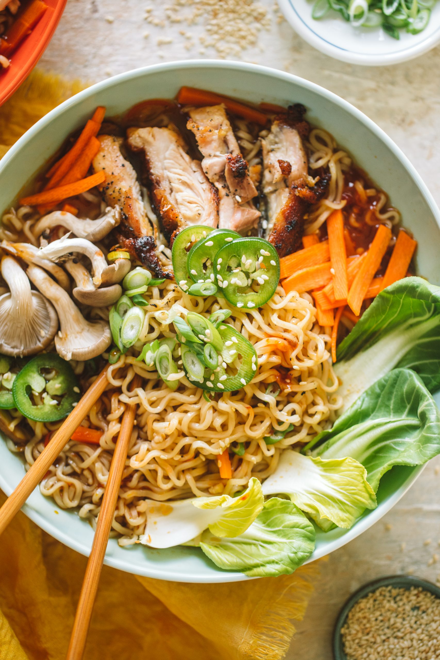 Spicy chicken ramen topped with jalapenos, mushrooms, bok choy, carrots and served in a blue bowl.