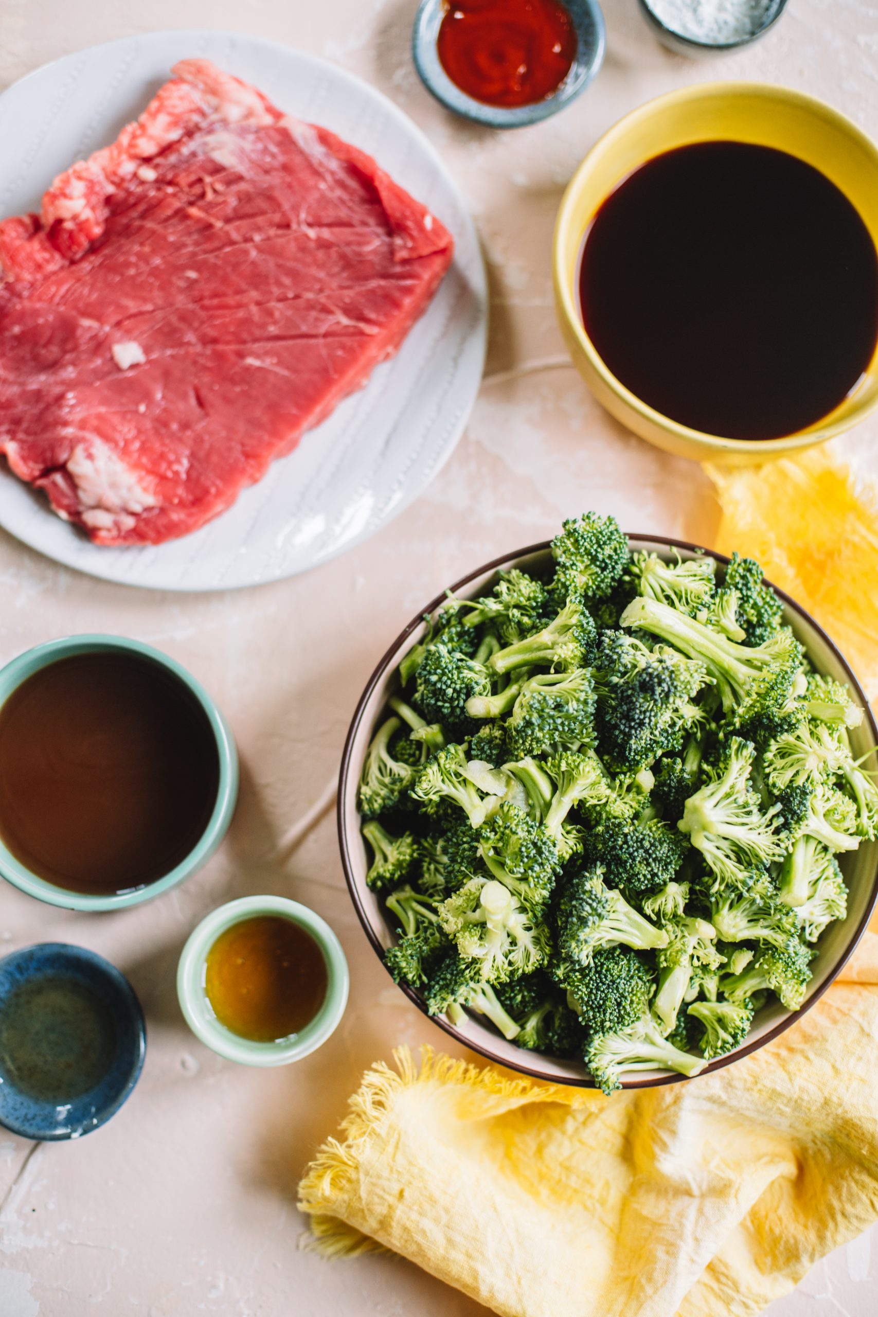 Flank steak, bowl of broccoli, soy sauce, sriracha, honey, sesame oil and beef broth bowls. 