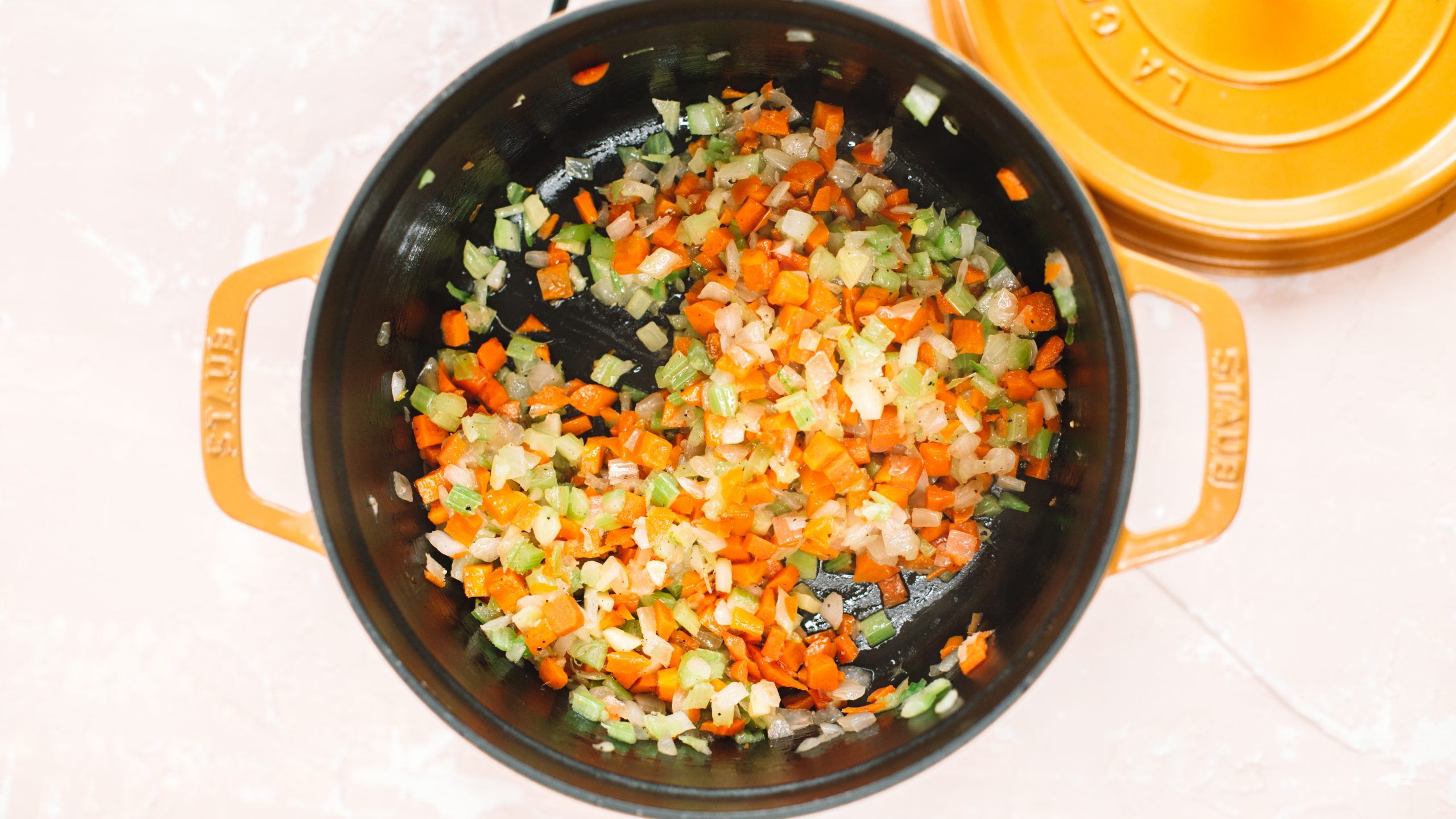 A dutch oven cooking celery, carrots and onion.