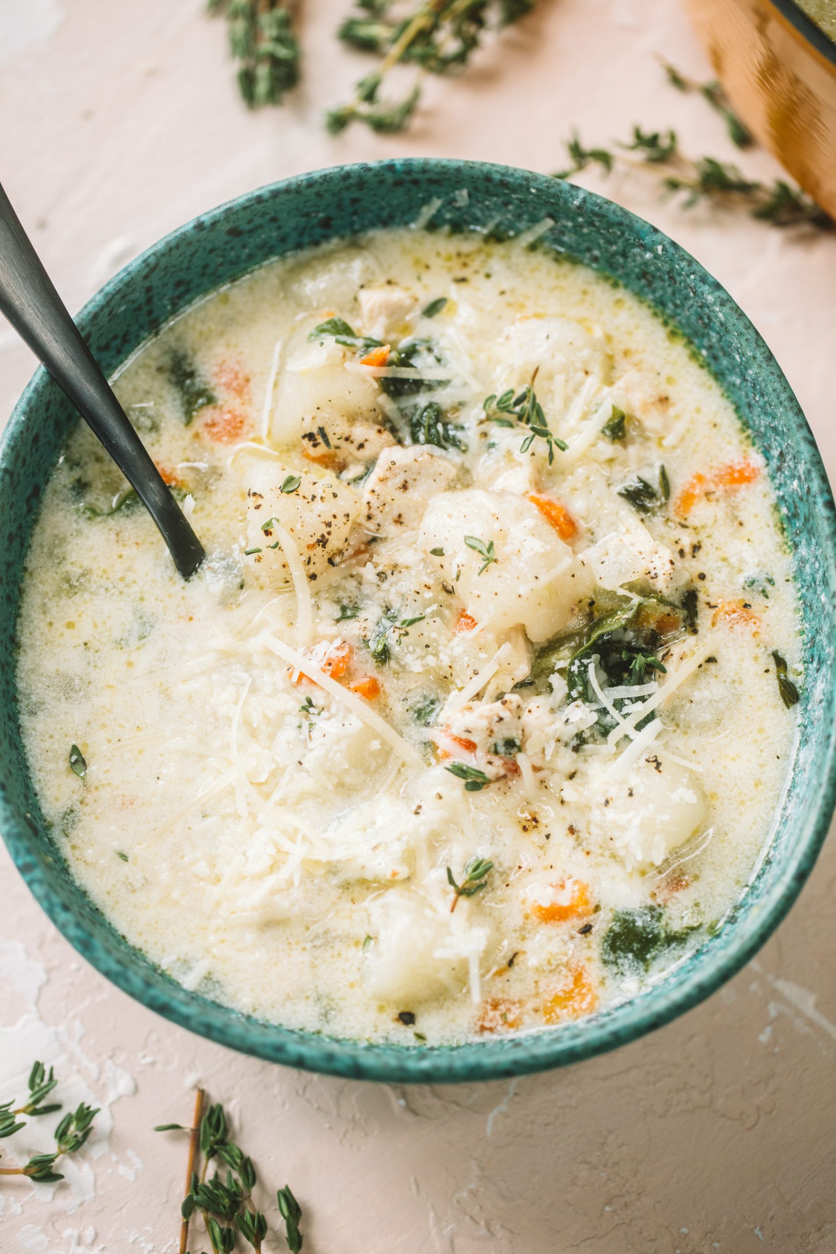 A bowl filled with creamy cauliflower gnocchi chicken soup and topped with parmesan cheese and fresh herbs. 