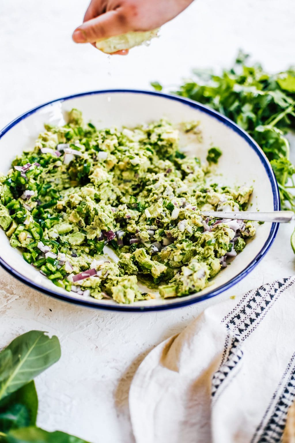 A large batch of guacamole with a lime being squeezed into the bowl. 