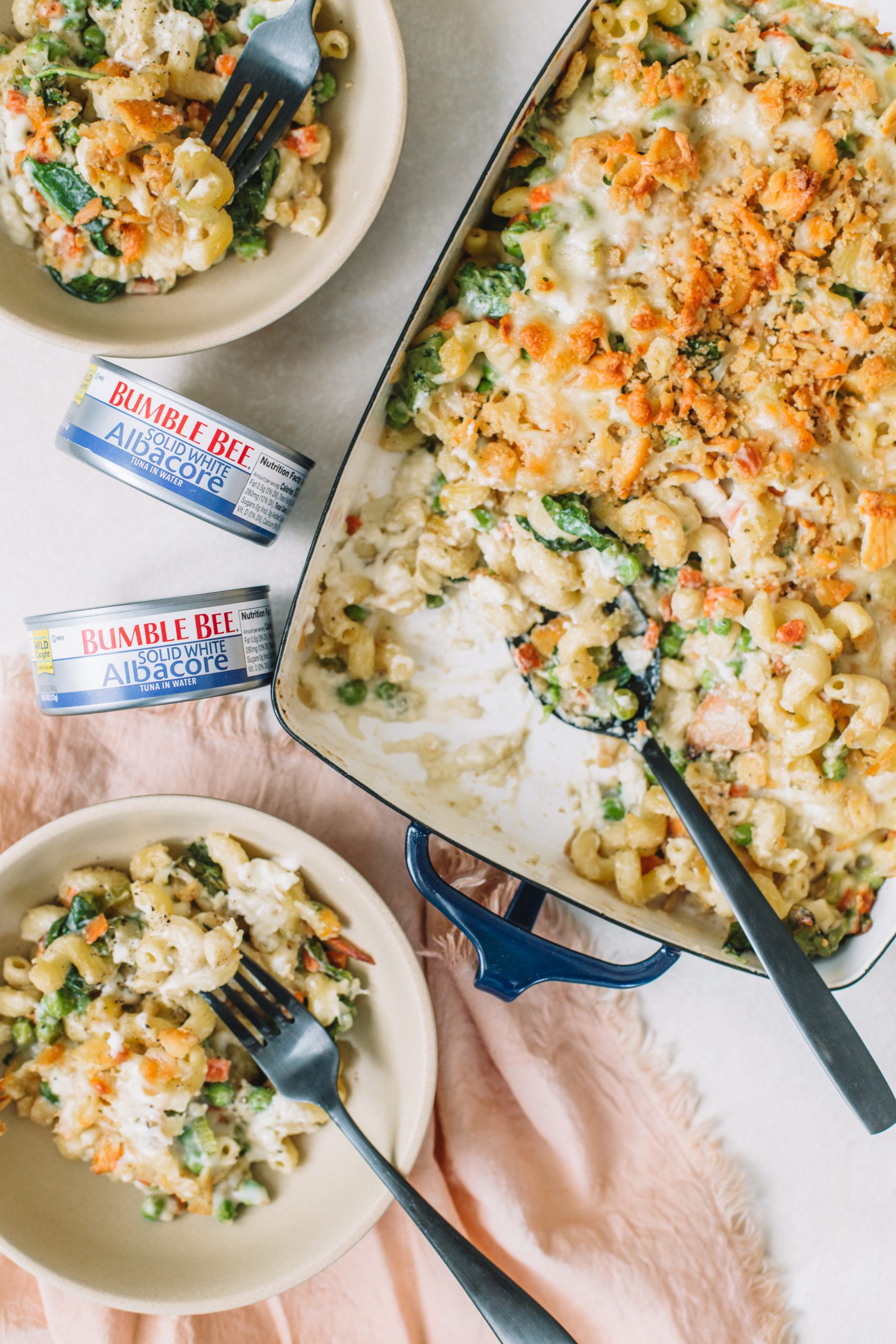 Tuna noodle casserole being served into tan bowls with a can of tuna.