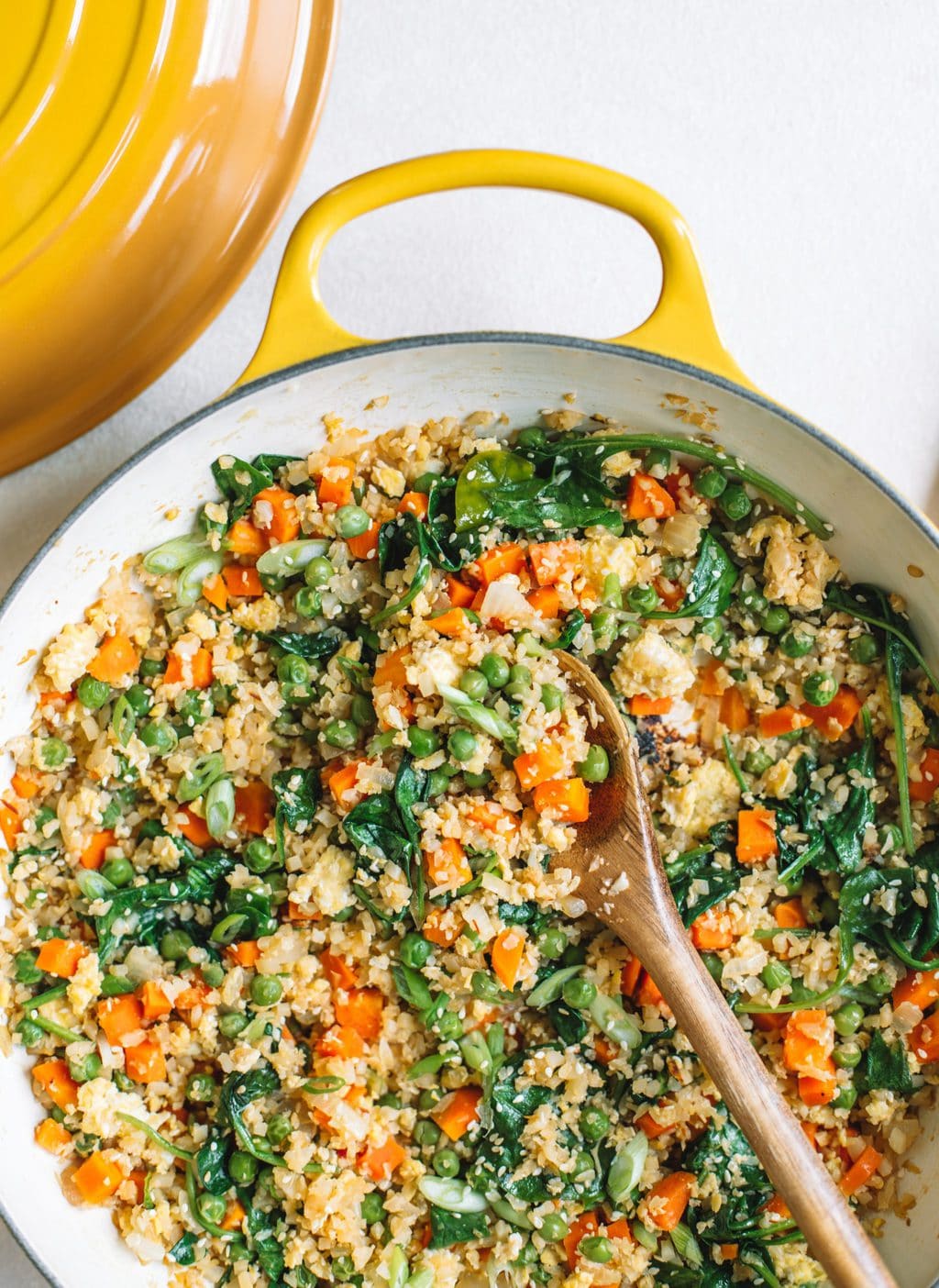 Cauliflower fried rice in a yellow skillet with a wooden spoon scooping a serving out. 