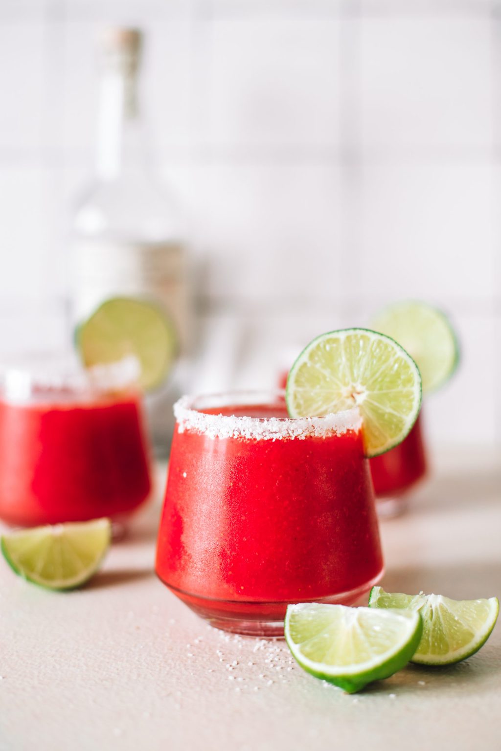 three glasses of blended strawberry margaritas with salt rim and lime wheel