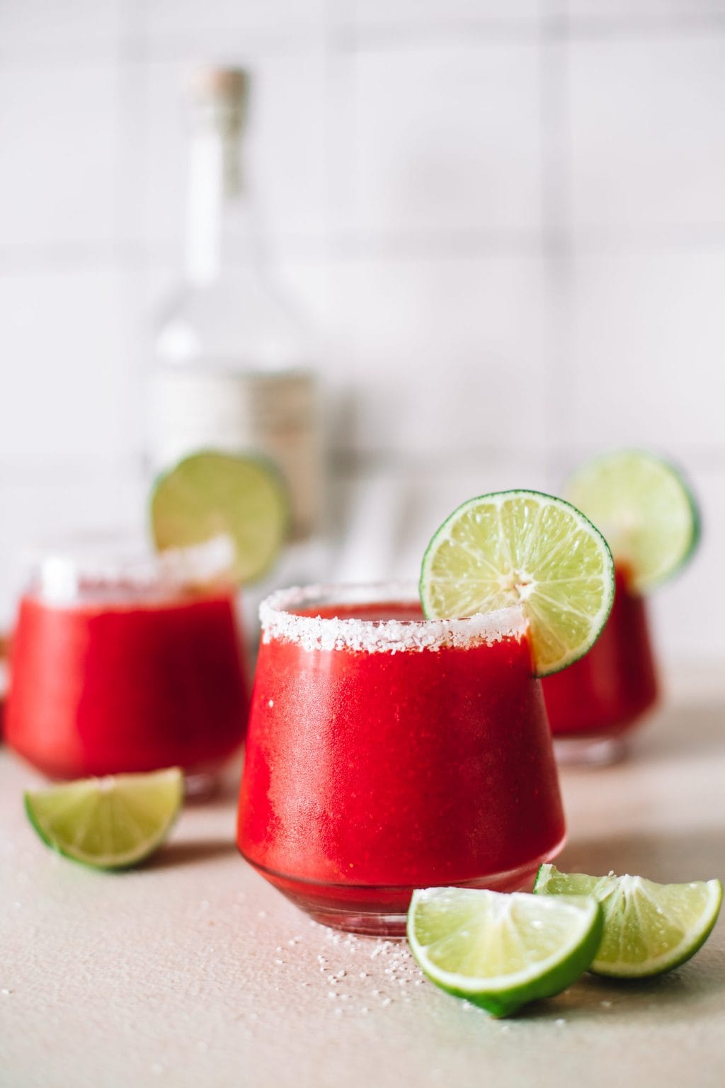 Frozen strawberry margaritas in a low clear glass garnished with a salt rim and lime wheel. 