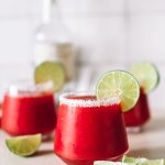 three glasses of blended strawberry margaritas with salt rim and lime wheel