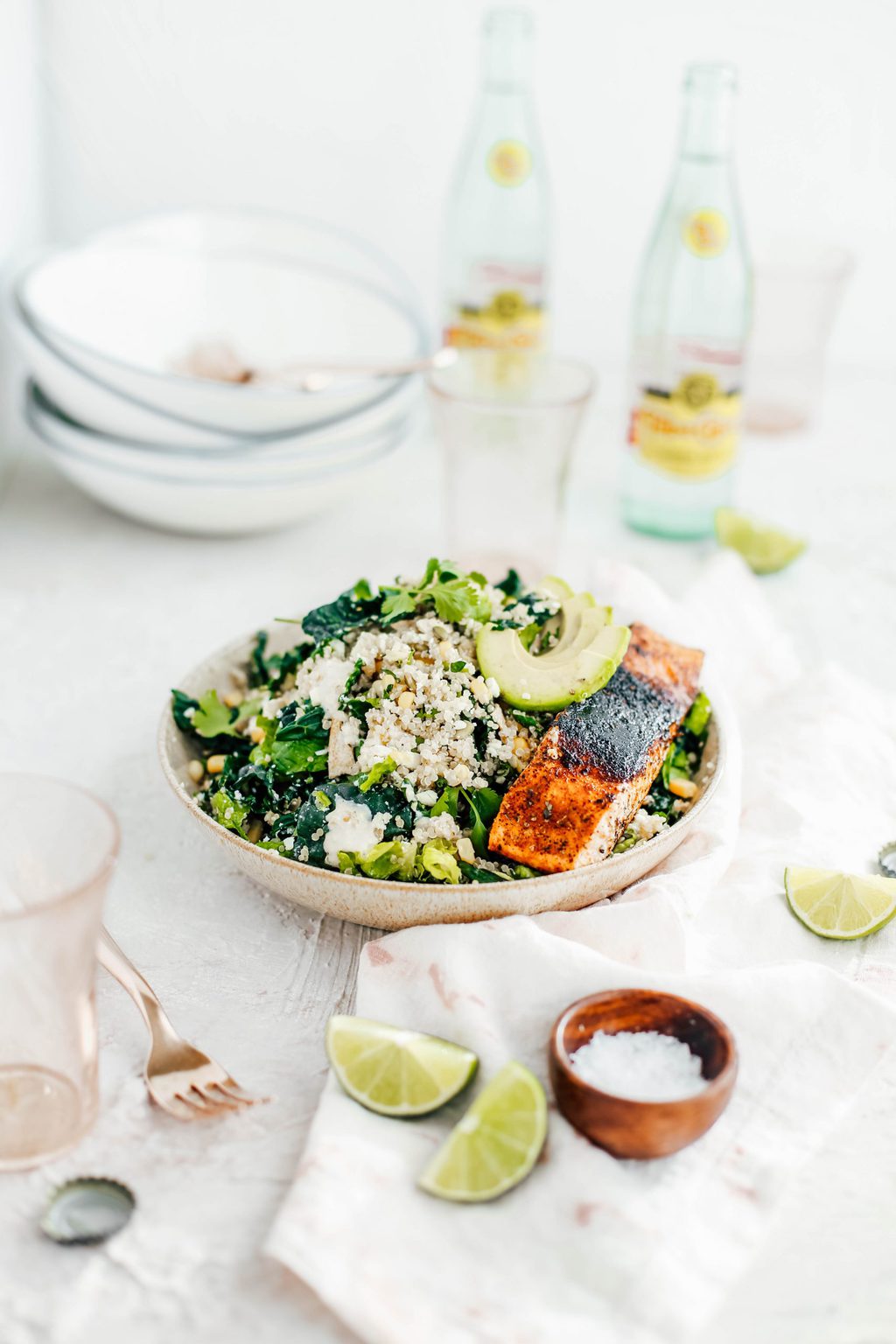 A mexican Cesar salad in a tan bowl topped with avocado slices and blackened salmon. 