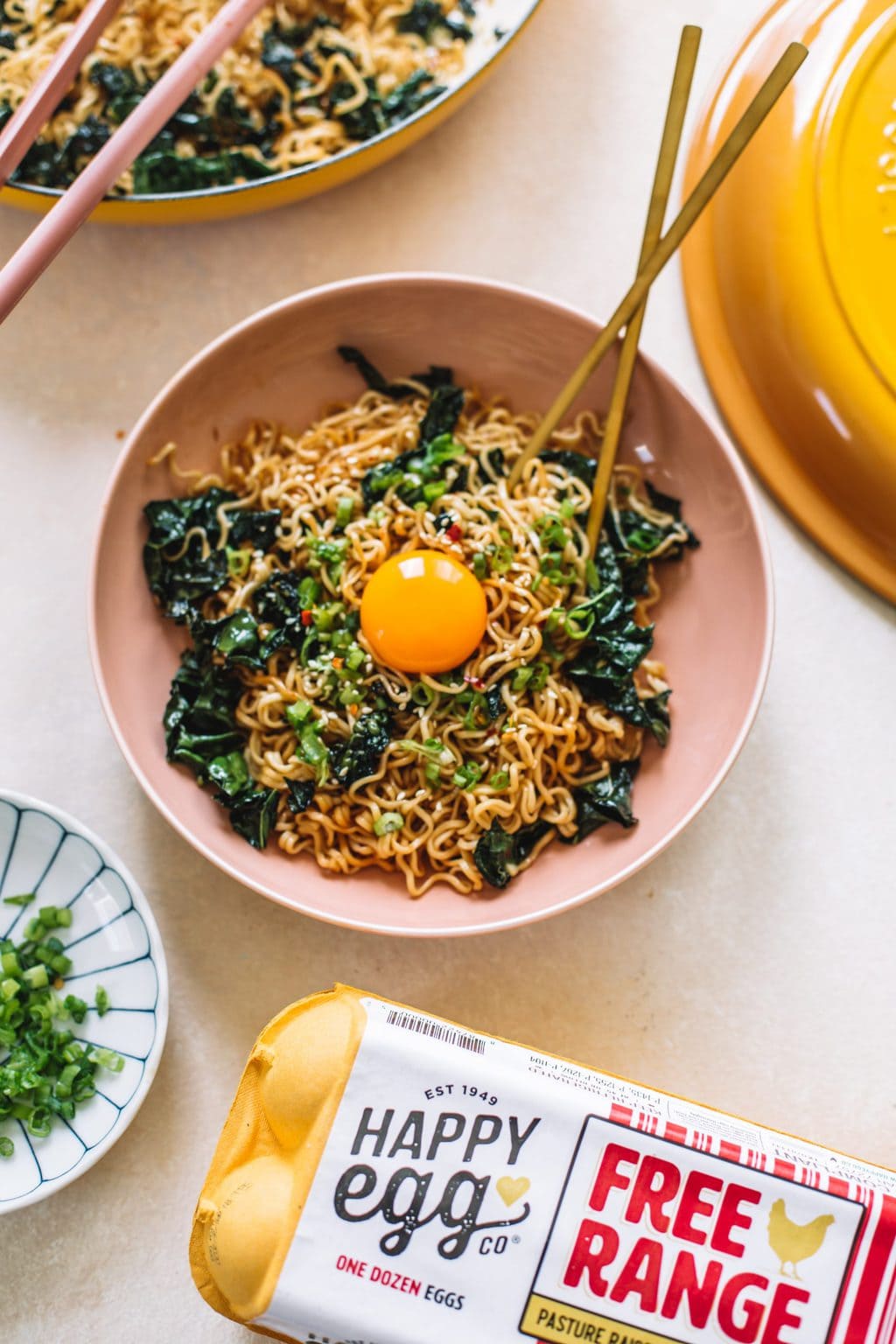 Garlic Butter Ramen Noodle Stir Fry served in a pink bowl with a side of green onions and an egg carton.