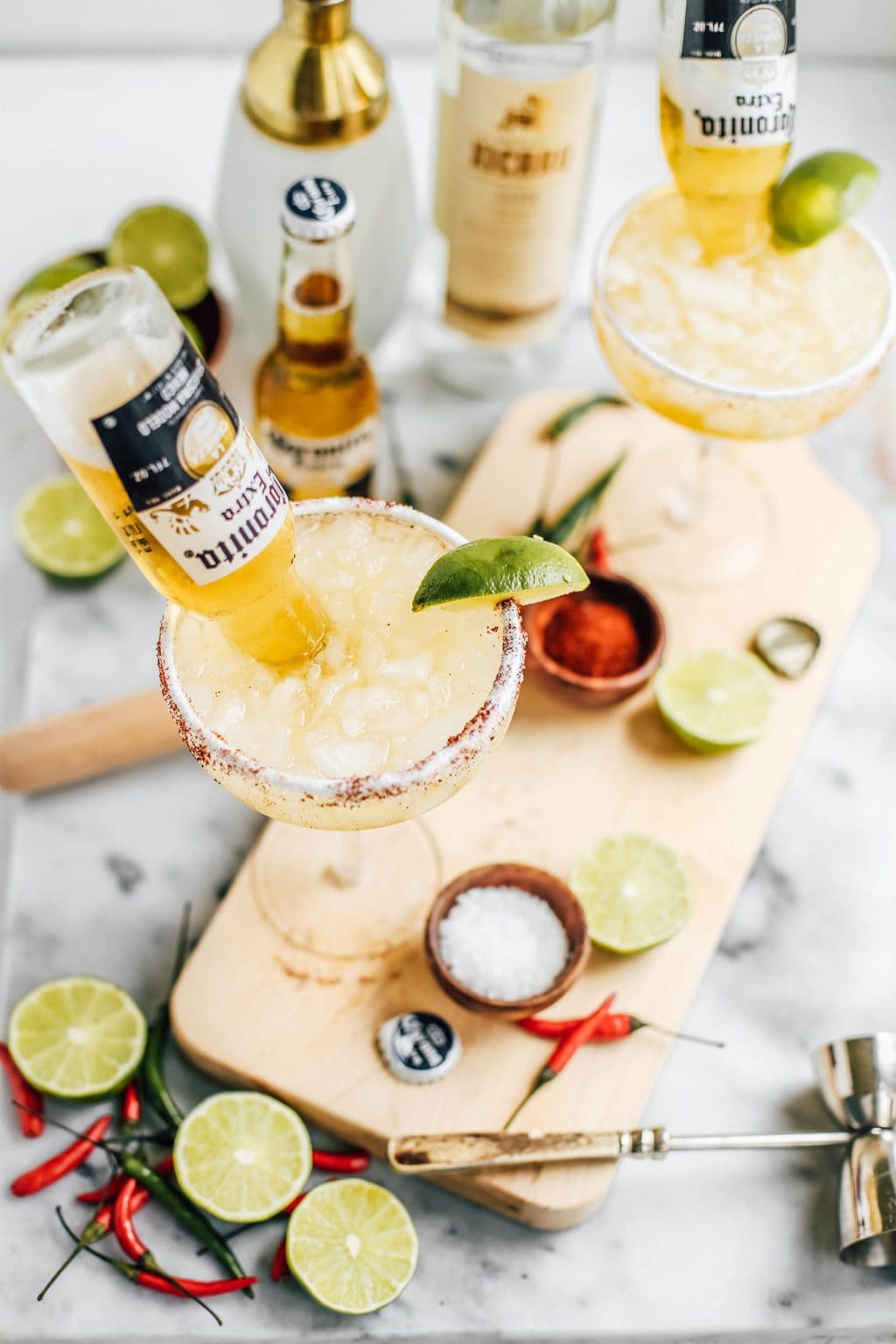 Small corona bottles being poured into a margarita glass. 