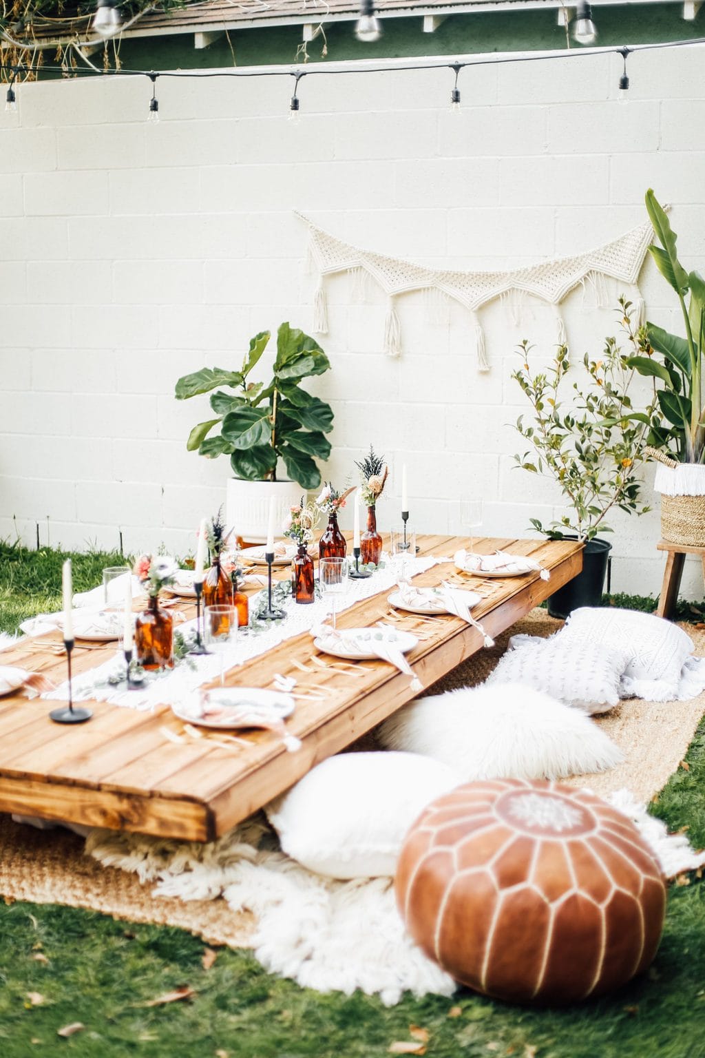 A dinner party setup in the middle of the backyard with plates, glassware and pillows as seats.