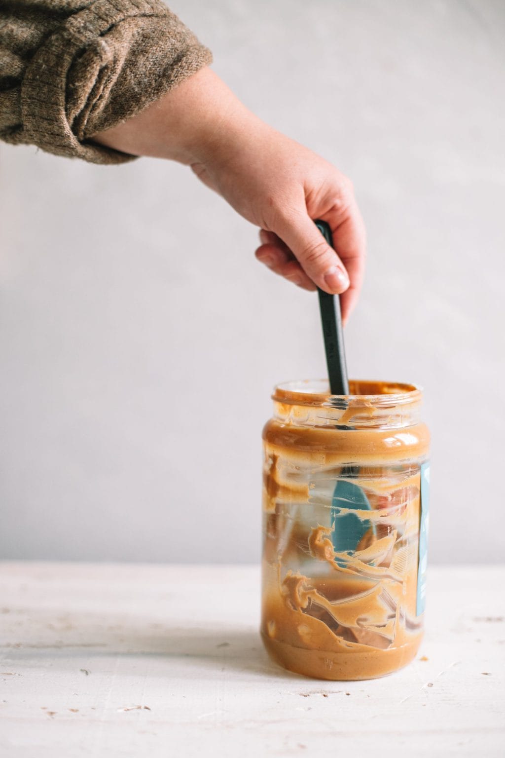 hand dipping spoon in empty peanut butter jar