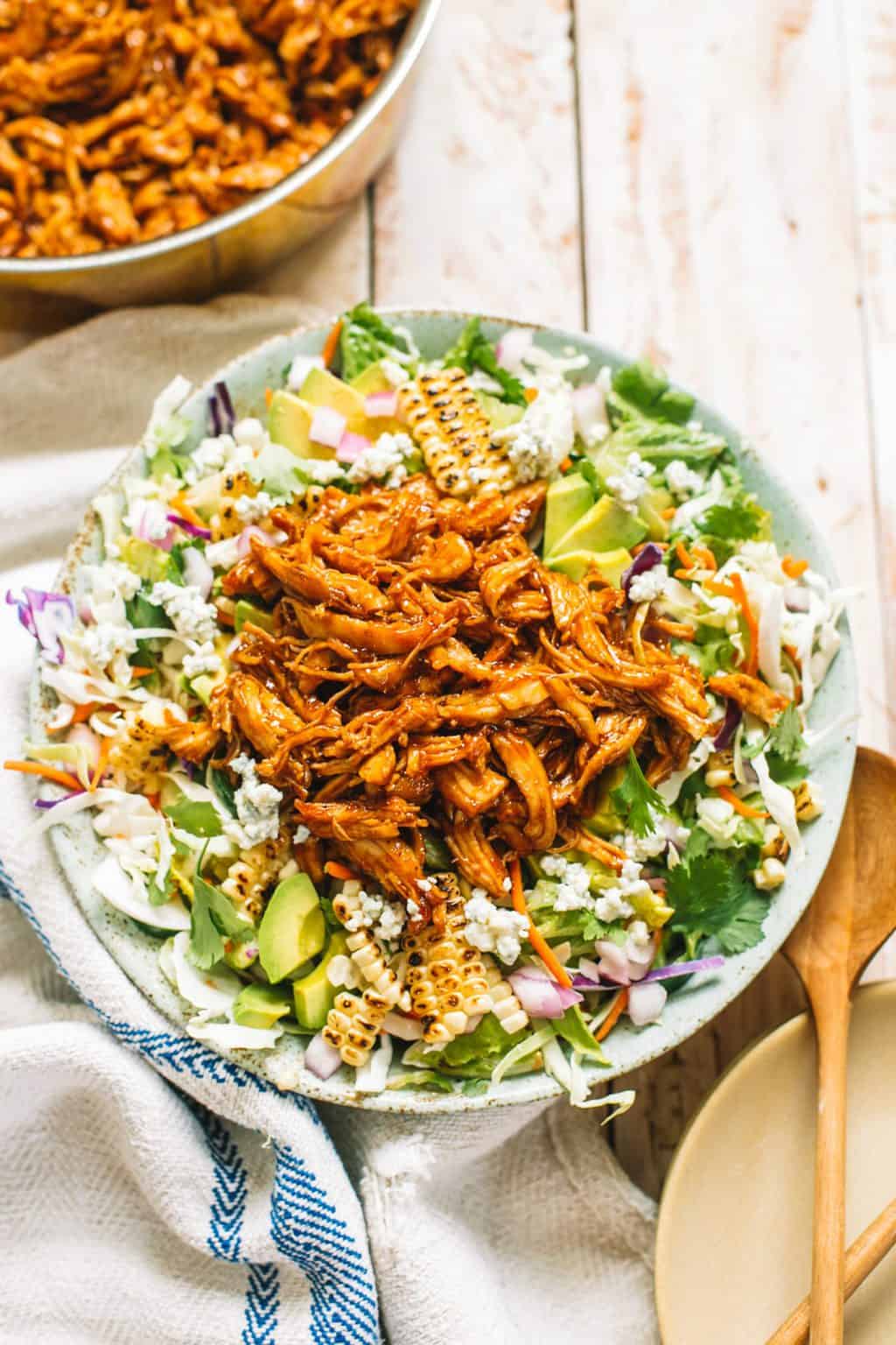 A blue bowl filled with coleslaw mixture topped with avocado and pulled bbq chicken.