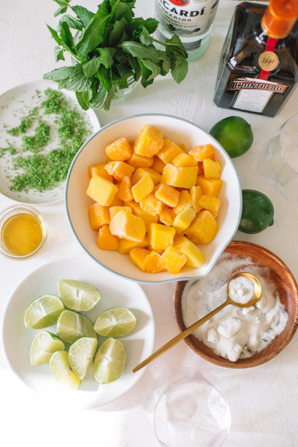 Bowls of frozen mango chunks, lime wedges, sugar and lime zest.