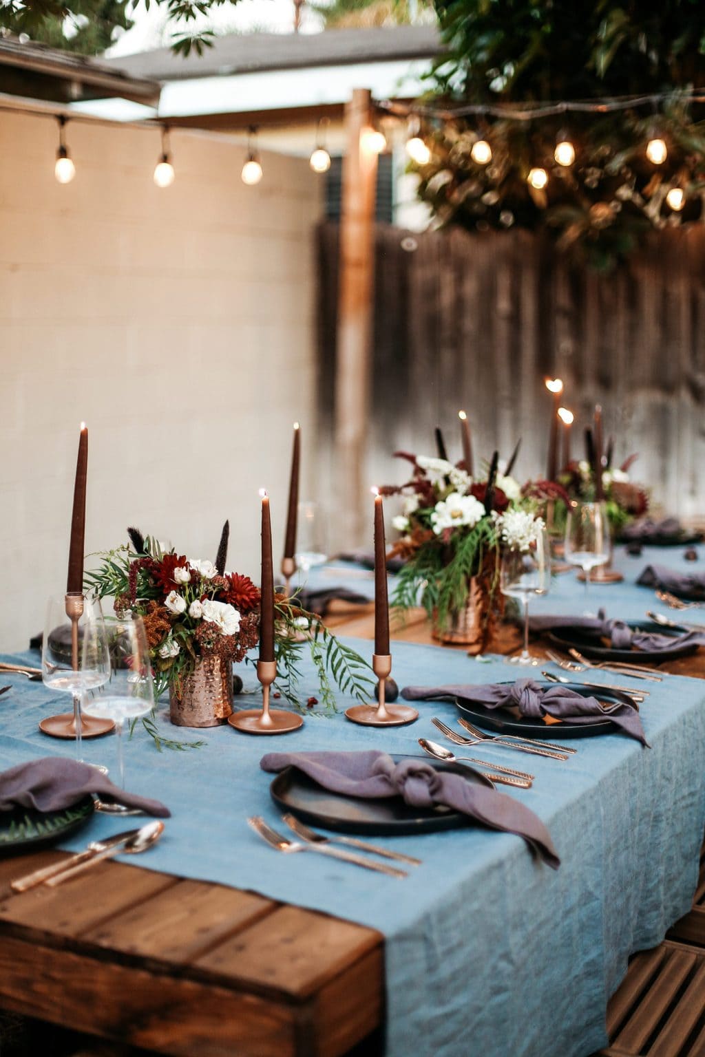 A moody dinner party set up with taper candles and string lights lit up.