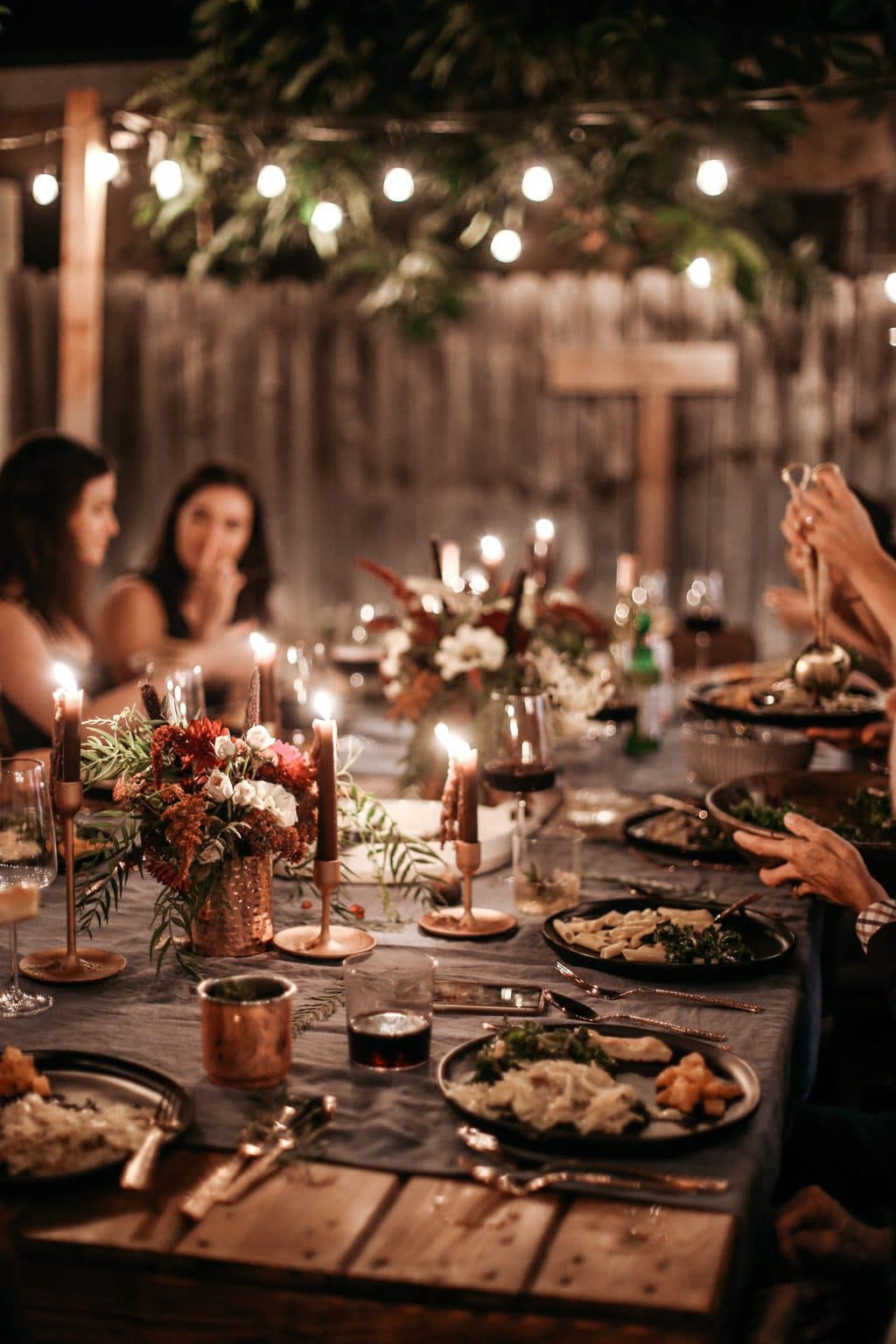 A dinner party at night with twinkle lights turned on overhead.