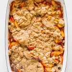 Peach cobbler in a navy blue casserole dish that has been baked.