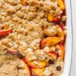 Peach cobbler that has been baked in a navy casserole dish.