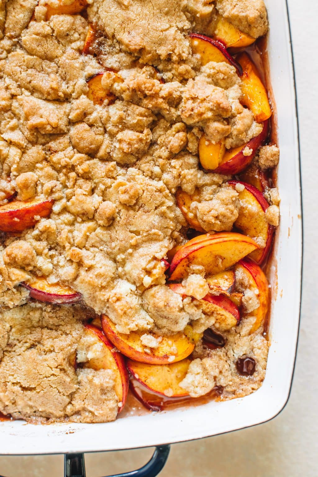 Peach cobbler that has been baked in a navy casserole dish.