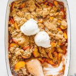 Peach cobbler in a navy blue casserole dish that has been baked and topped with vanilla ice cream.