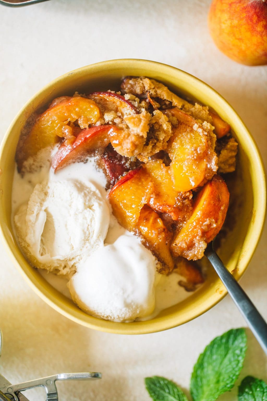 Peach cobbler served in a small yellow bowl with two scoops of vanilla ice cream.