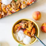 Peach cobbler served in a small yellow bowl with two scoops of vanilla ice cream.