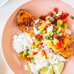 Salmon topped with pineapple glaze sitting on a bed or rice with pineapple salsa in a pink bowl.