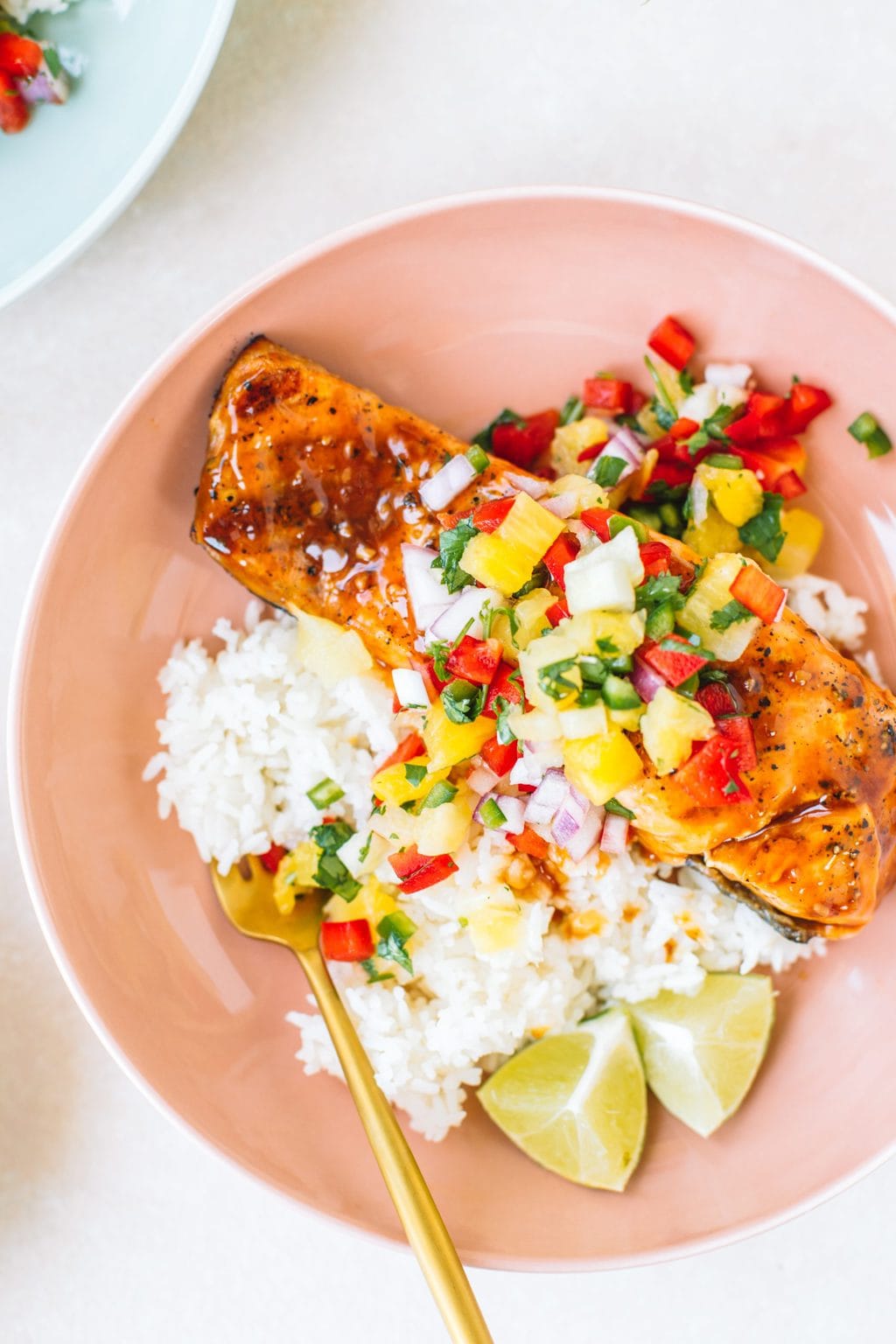 Salmon topped with pineapple glaze sitting on a bed or rice with pineapple salsa in a pink bowl.