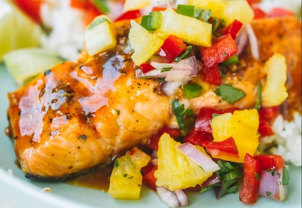 Salmon filet with pineapple glaze and topped with pineapple salsa in a blue bowl.