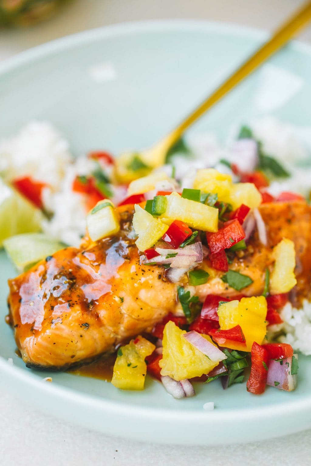 Salmon filet with pineapple glaze and topped with pineapple salsa in a blue bowl.