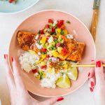 Salmon topped with pineapple glaze sitting on a bed or rice with pineapple salsa in a pink bowl.