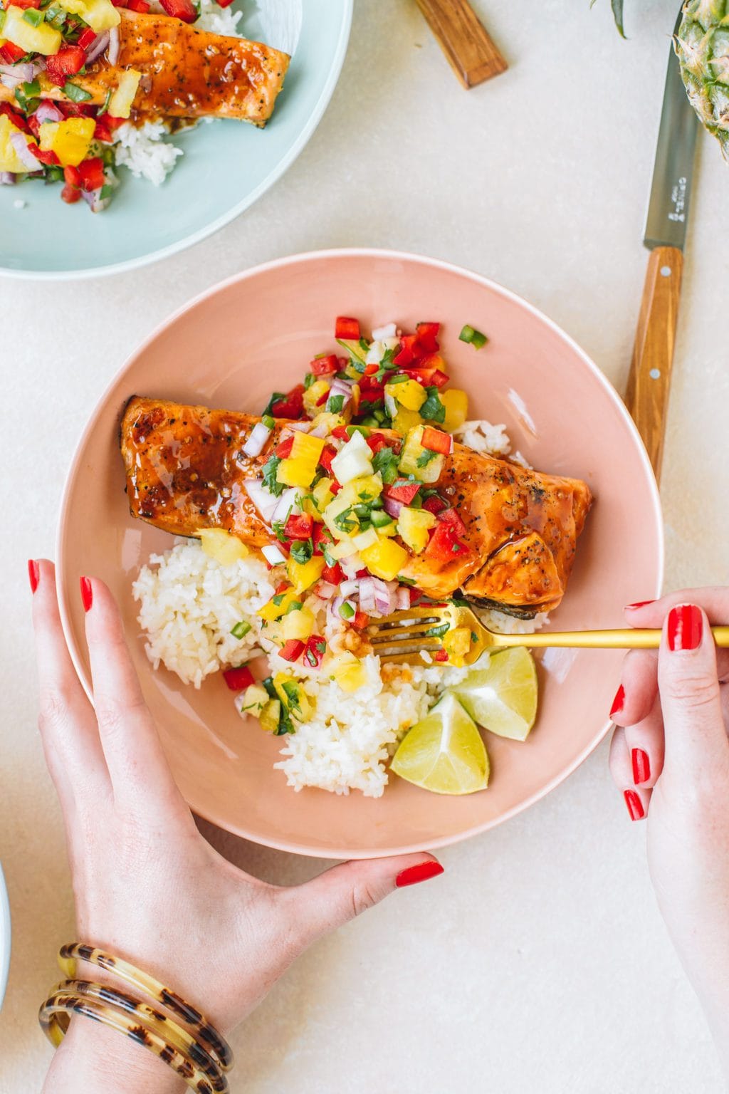 Salmon topped with pineapple glaze sitting on a bed or rice with pineapple salsa in a pink bowl.