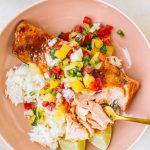 Salmon topped with pineapple glaze sitting on a bed or rice with pineapple salsa in a pink bowl.