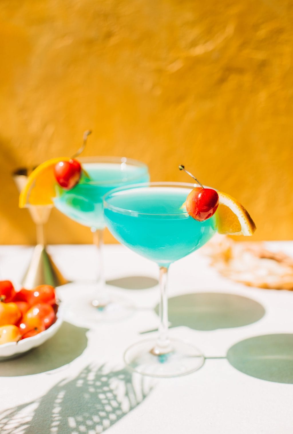 two blue lagoon cocktails in coupe glasses with cherries and orange slices