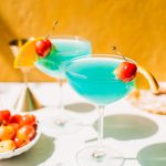 two blue lagoon cocktails in coupe glasses with cherries and orange slices