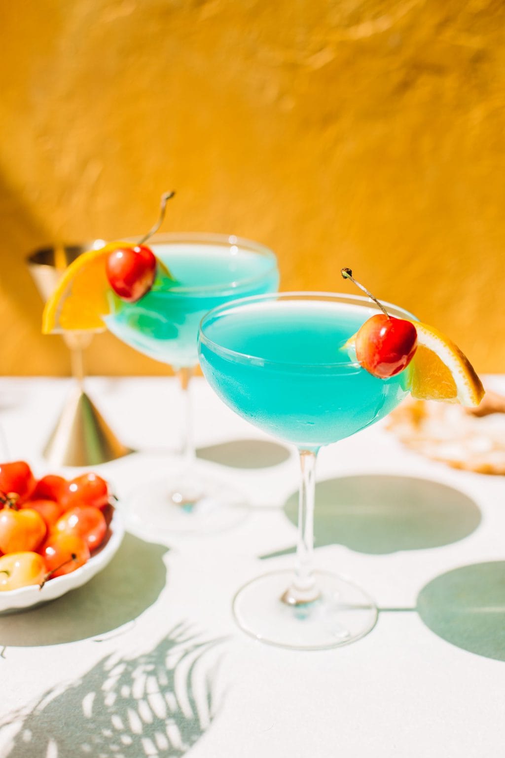 two blue lagoon cocktails in coupe glasses with cherries and orange slices