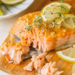 flaked salmon fillet topped with lemon slices and fresh thyme on cedar wood plank